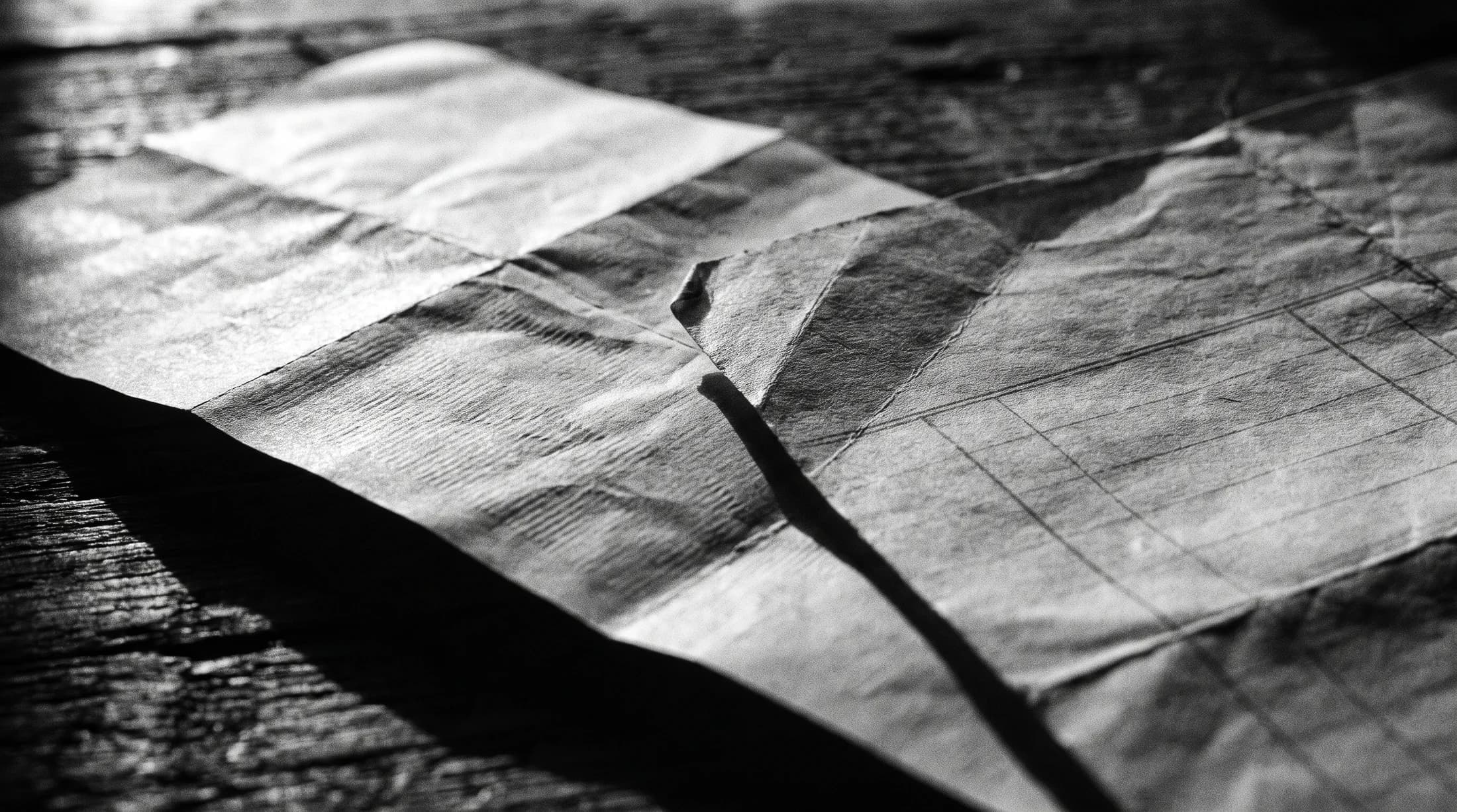 Macro detail of folded receipt paper and a creased printed ledger in raking light